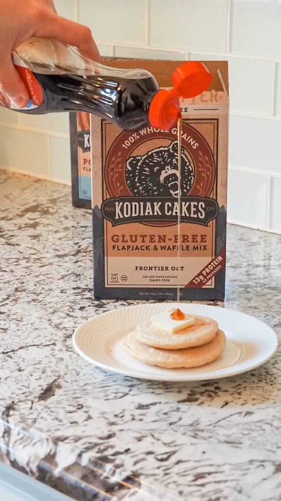 Syrup pouring onto a stack of Kodiak Cakes pancakes with butter