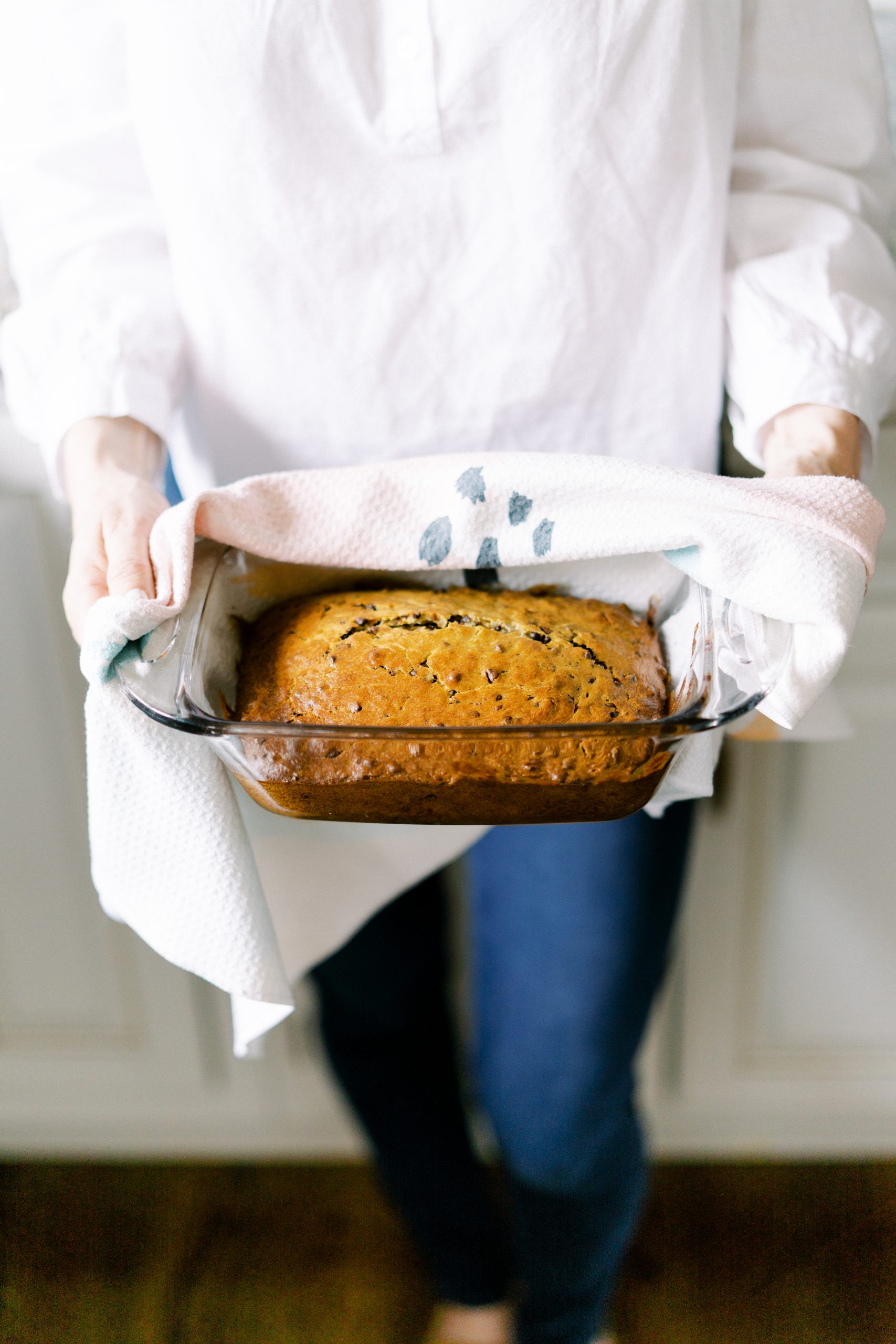 woman holding warm chocolate chip banana bread in a loaf pan